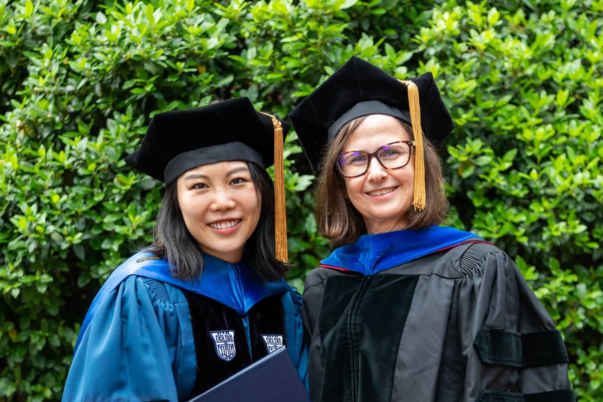 Two women in cap and gown, one with diploma