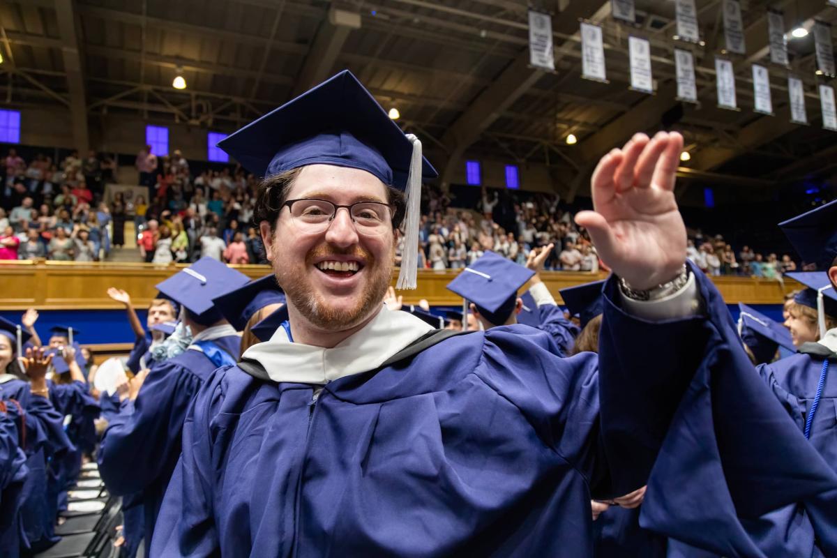 Man smiling at graduation, waving