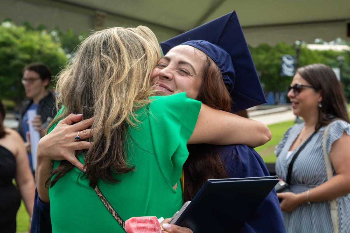 Woman in cap and gown smiling and hugging someone