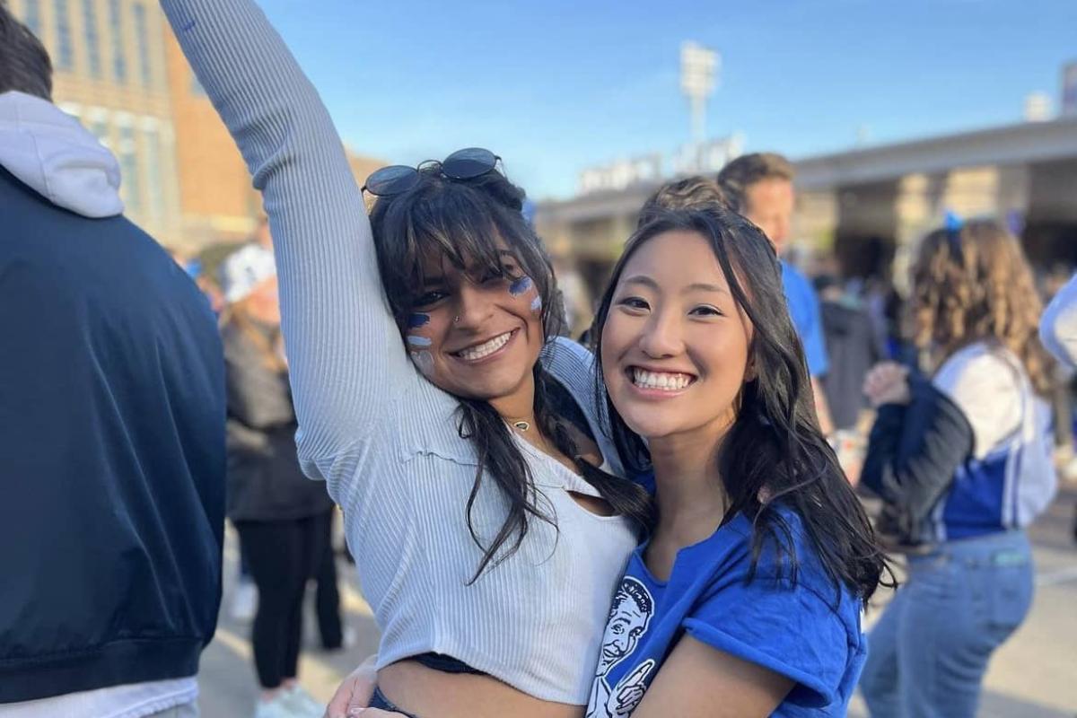 Two woman cheering and happy, hugging, one with arm above her head.