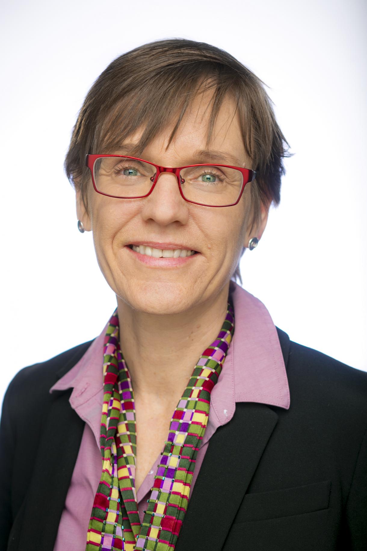 Woman, short hair and red glasses, bright blouse and scarf, smiling