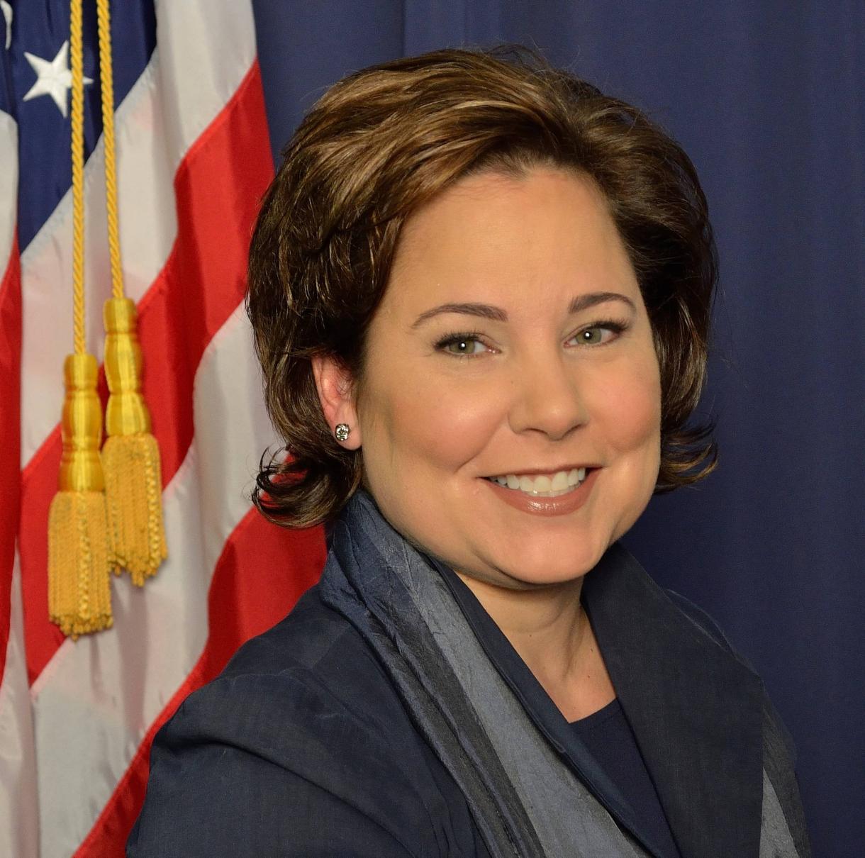 woman, suit, American flag behind her