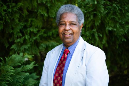 Man, smiling, suit and bright tie. In front of green trees