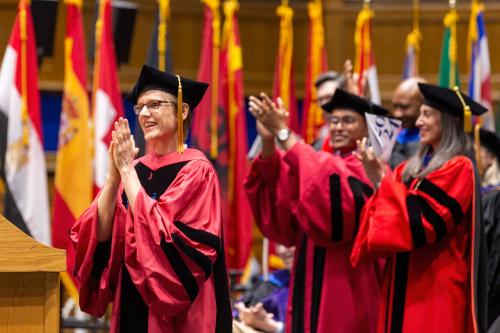 Woman smiling and looking caring in cap and gown, others behind her chering