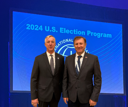 Two men in suits standing side-by-side in front of a blue screen