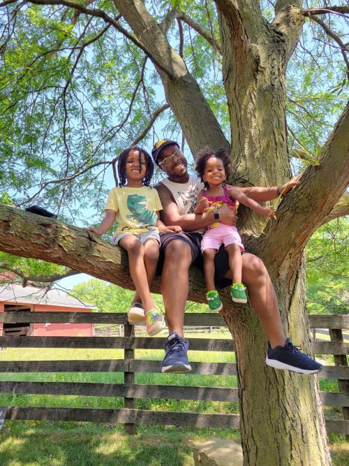 Man with two small children sitting on a tree together. 